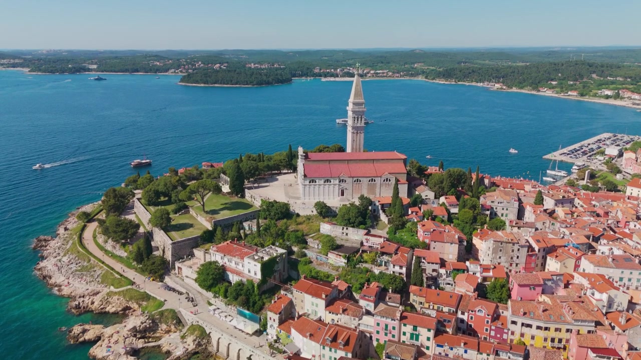 Drone che vola verso il centro storico di Rovigno e la chiesa di Sant'Eufemia, rivelando la penisola, i tetti in terracotta e la costa adriatica sotto la luminosa luce estiva.