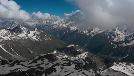 Air-flight-through-mountain-clouds-over-beautiful-snow-capped-peaks-of-mountains-and-glaciers.