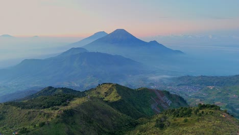 aerial view of green lush mountain range with layers of misty hills and dramatic peaks illuminated by golden morning light on the background. mt prau with mt sindoro and mt sumbing scenery, indonesia