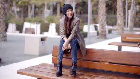 Fashionable-young-woman-sitting-waiting-on-a-bench