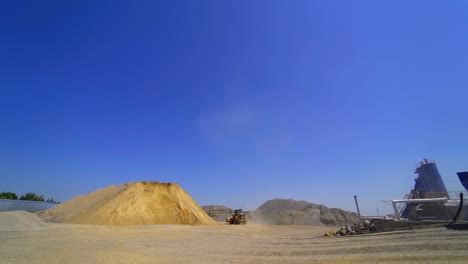 new asphalt factory in summertime. excavator transports sand and gravel on outdoor industrial plant.