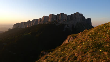 Sharp-jagged-granite-cliffs-illuminated-by-golden-hour-dusk-glow-on-grassy-hillside