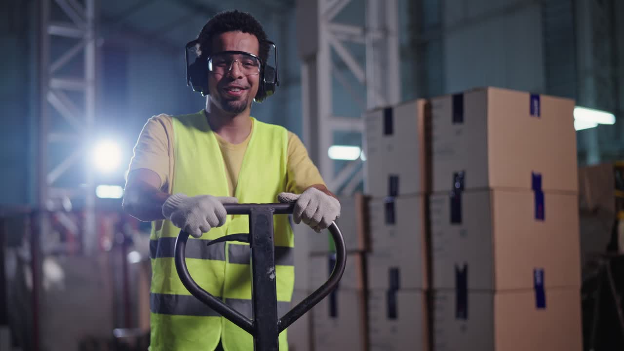 Man in safety gear smiling in a warehouse with a pallet jack