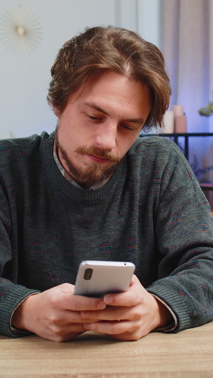 Homem caucasiano barbudo sentado à mesa usa smartphone para compartilhar mensagens em aplicativos de mídia social