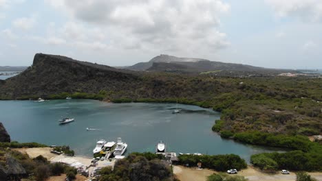 Tugboat-beach-in-curacao-with-boats-on-clear-waters-and-rugged-hills,-aerial-view