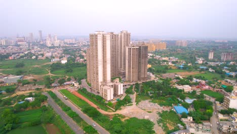 aerial drone shot flying towards under construction building in the middle of green fields showing the rapid growth of multistory high rise houses and offices