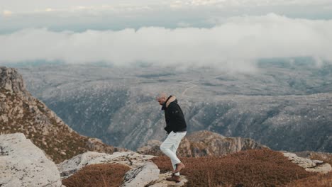 Man-slowly-walking-with-his-hands-in-his-pockets,-then-climbing-a-rock-and-looking-at-the-horizon