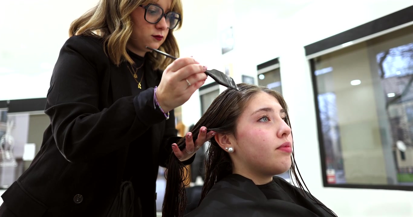 Parrucchiere professionista che applica la tinta ai capelli di una cliente in salone