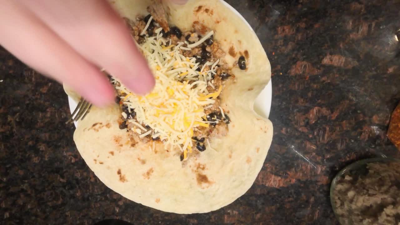 Top down close up view of chef putting cheese onto a homemade beef tortilla wrap in a kitchen