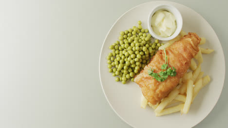 Video-of-fish,-chips-and-peas-on-plate-with-dip,-with-copy-space-on-white-background