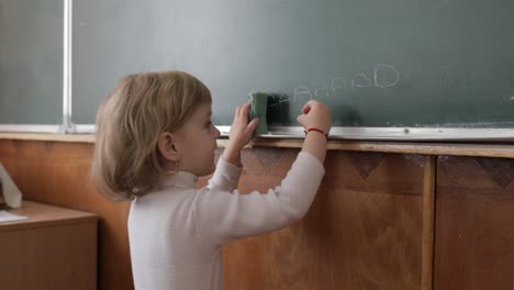 girl drawing at blackboard using a chalk in classroom. education process