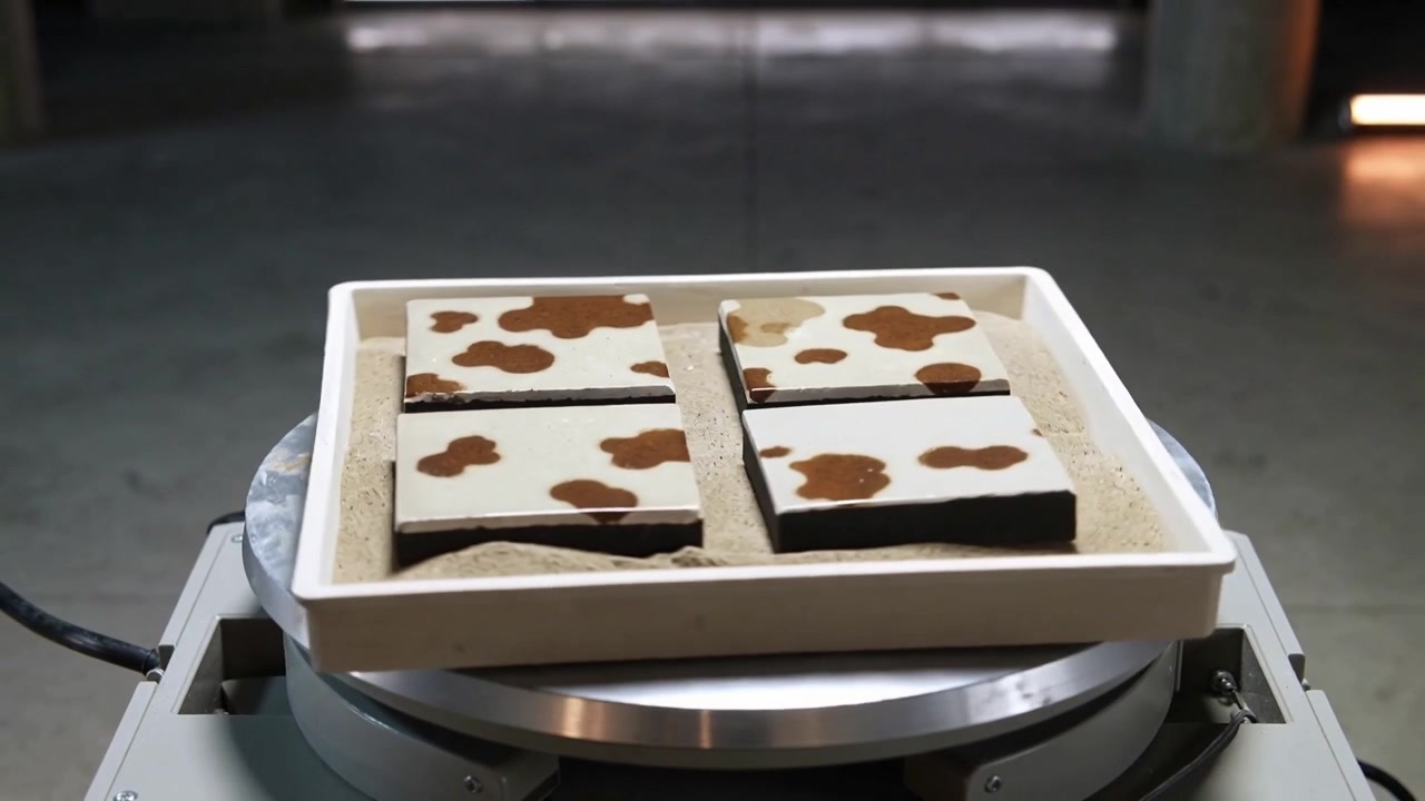 Power cable driving turntable rotating white tray with sand in workshop, revealing brown tile edges
