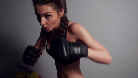 close up view of a young woman in boxing gloves punching bag in dark fitness studio. boxing in slow motion