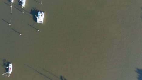 overhead shot of small boats floating in the brown brisbane river casting long shadows