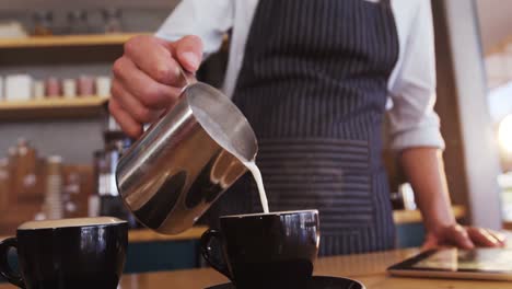 camarero vertiendo leche en la taza de café mientras prepara el café