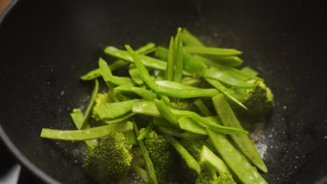 anonymous cook adding cut bell beans to broccoli in pan