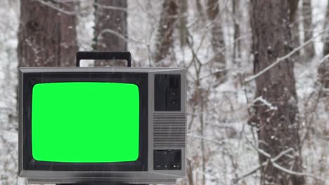 vintage tv with green screen in the forest in winter season while is snowing