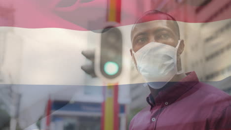 animation of flag of netherlands waving over man wearing face mask during covid 19 pandemic