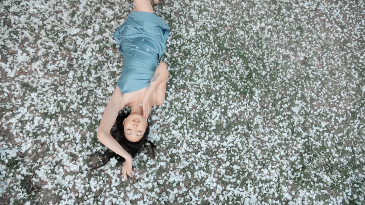 Woman in a light blue dress lying on a bed of cherry blossoms