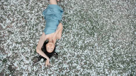 woman in a light blue dress lying on a bed of cherry blossoms