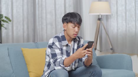 집 의 거실 의 소파 에 앉아 스마트폰 을 사용 하는 지루 한 아시아 청소년 소년