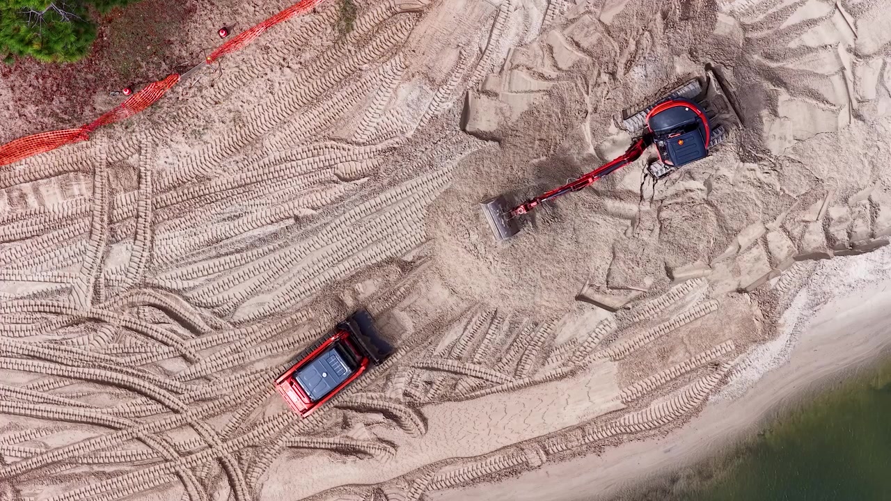 Top-down aerial shot of heavy machinery moving sand for coastal management on a beach
