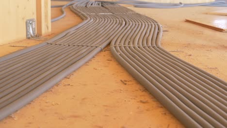 close up: grey corrugated tubing runs along the wooden floor of unfinished house