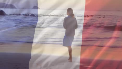 animation of flag of france over caucasian woman walking at beach