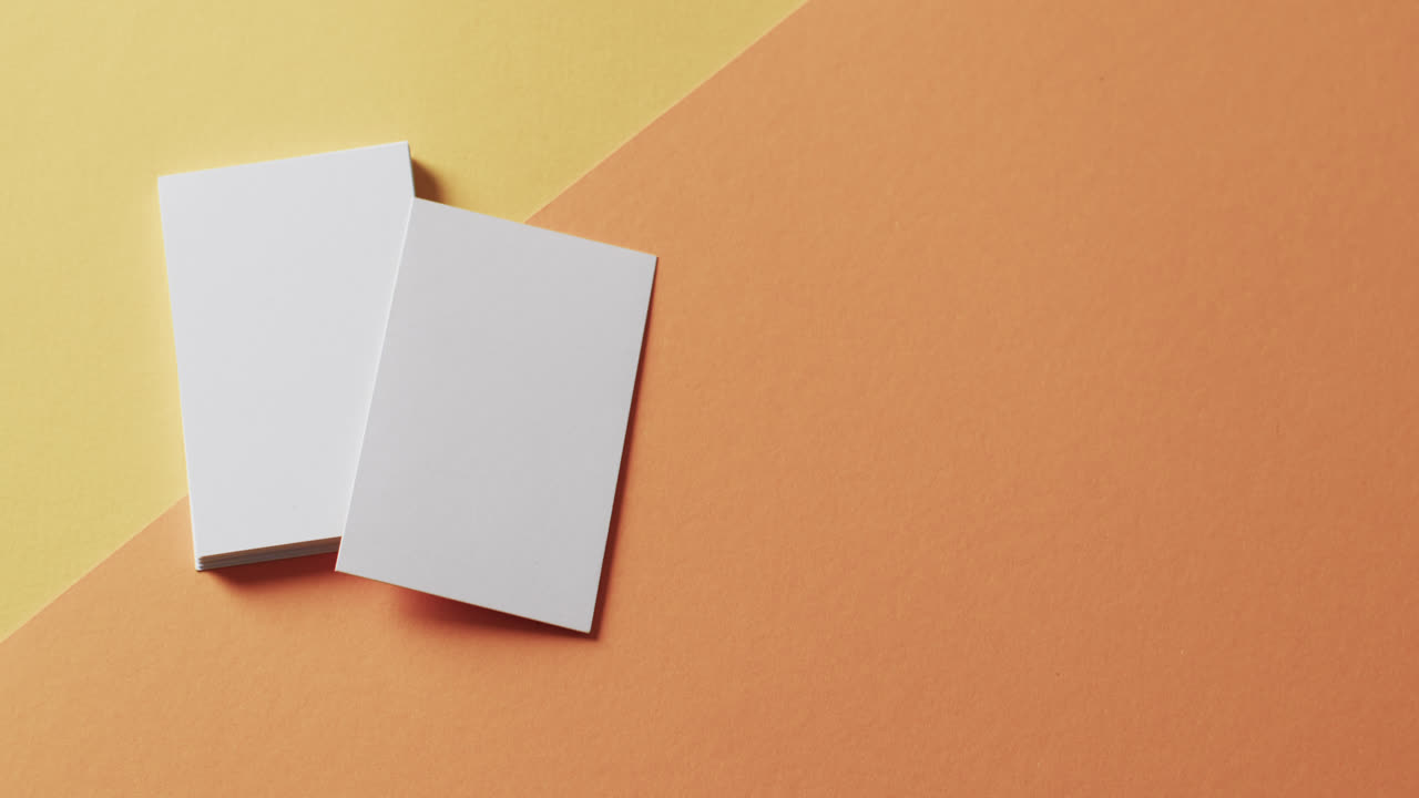Overhead view of blank white business cards on yellow and orange background, copy space, slow motion