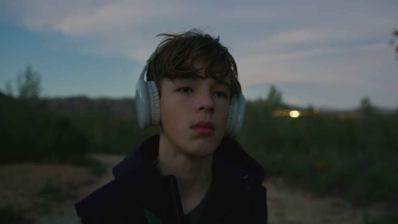 мальчик-подросток слушает музыку на открытом воздухе в сумерках