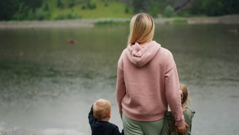 mother and little children enjoy calm lake standing on bank