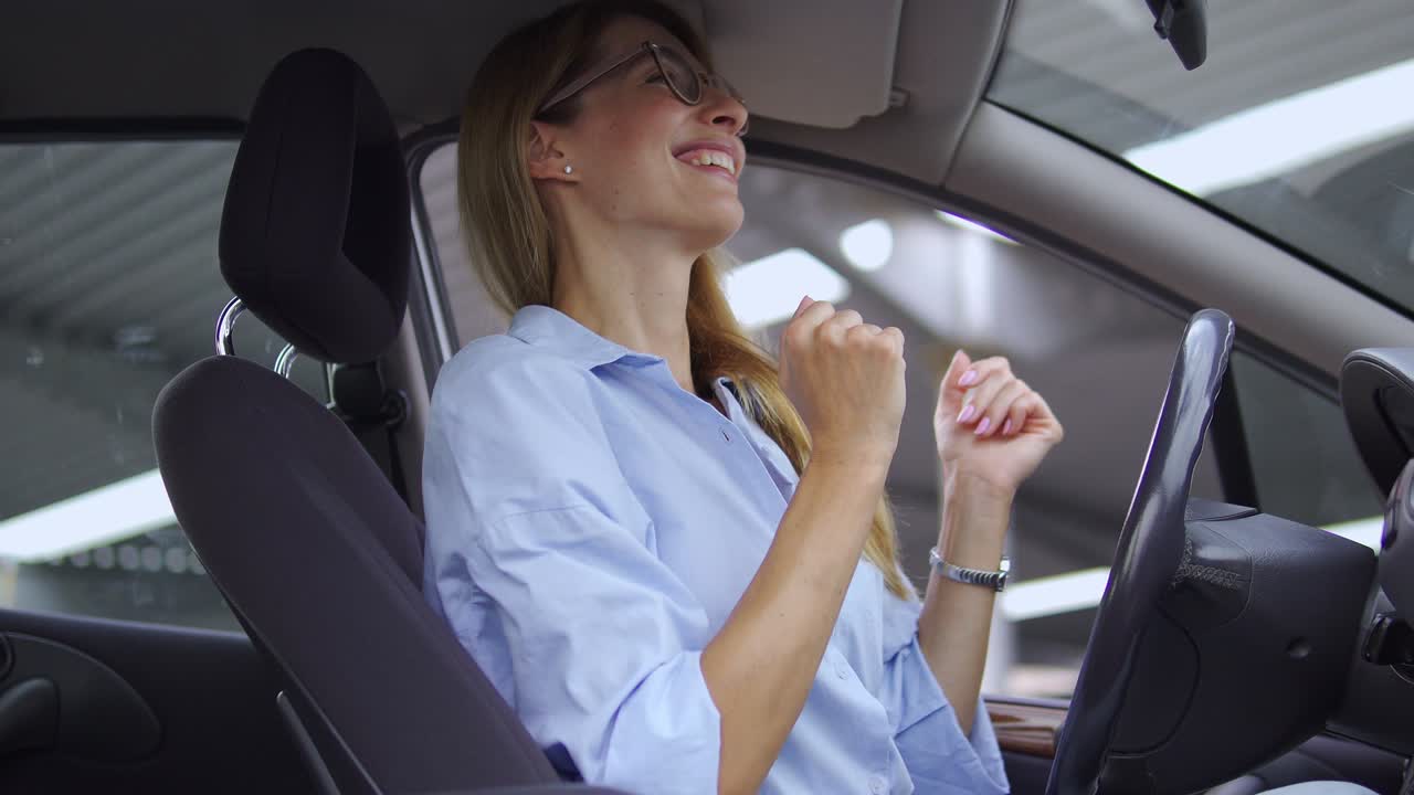dama rubia alegre en camisa casual bailando baile activo y positivo sentada en el asiento del conductor en su coche, disfrutando de la música y moviéndose rápidamente, celebrando la apertura de su propio negocio, el éxito