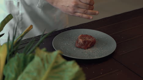 Close-up-of-gourmet-meat-dish-on-wooden-table,-chef-adding-salt-and-spices