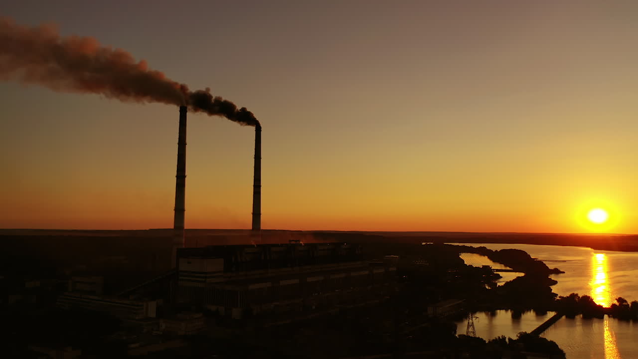 Harmful factory among nature at sunset. Dangerous smoke fills the air from industrial pipes. Manufacturing at dusk. Environment in danger. Global warming.