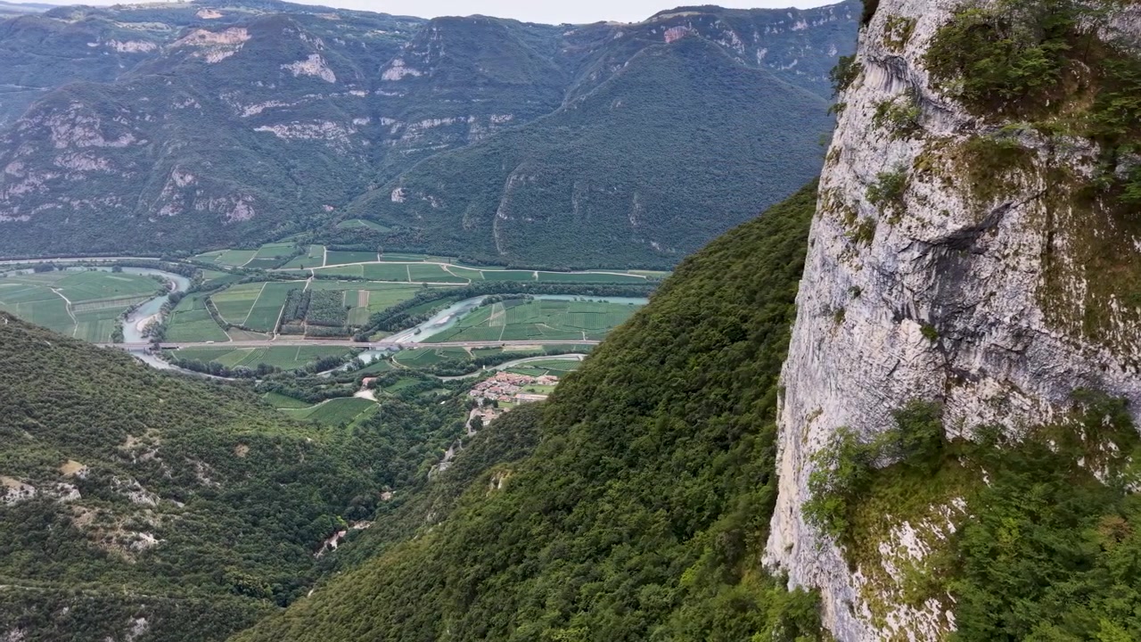 Vue de drone depuis le côté opposé du Sanctuaire Madonna della Corona, surplombant une vallée luxuriante, des falaises spectaculaires et une autoroute sinueuse dans le nord de l'Italie