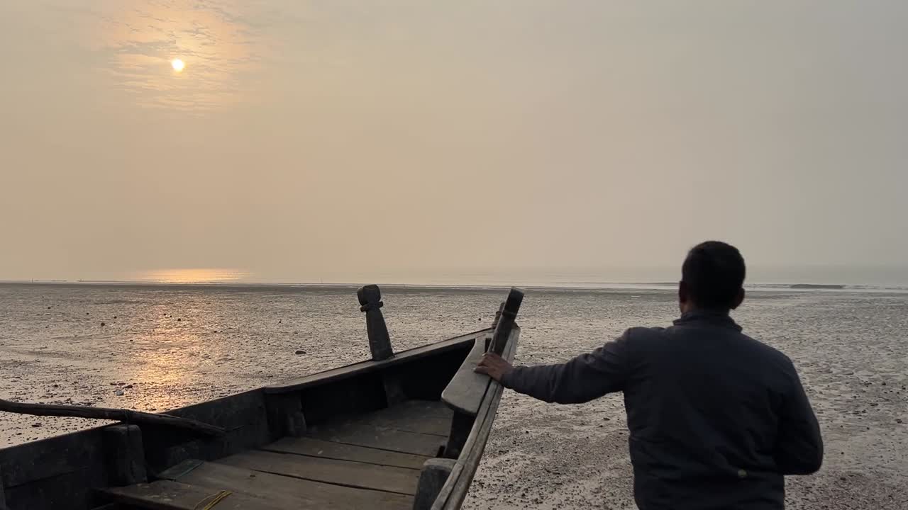 Close up rear shot of a man holding an Indian fishing boat during sunset at a beach in Bengal , India