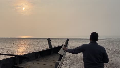 Primer-Plano-Trasero-De-Un-Hombre-Sosteniendo-Un-Barco-Pesquero-Indio-Durante-La-Puesta-De-Sol-En-Una-Playa-En-Bengala,-India