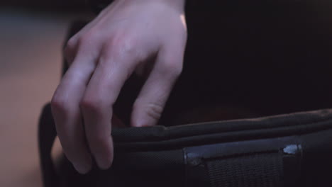 Close-up-of-hands-opening-zipper-of-bag-and-pulls-on-leather-gloves-in-basement