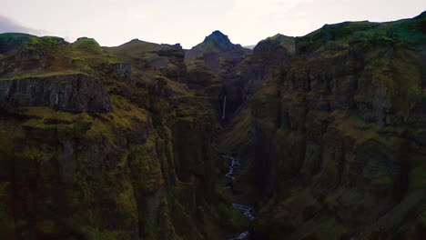 Turista-Caminando-Cerca-Del-Cañón-Mulagjufur-En-Islandia-Con-Vista-Lejana-De-La-Majestuosa-Cascada-Entre-Rocas-En-Un-Día-De-Mal-Humor