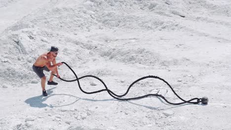 athletic strong man doing exercises with ropes outdoors on the sand. shirtless bodybuilder training