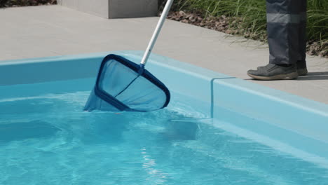 a worker removes debris from a pool with a net. close-up shot