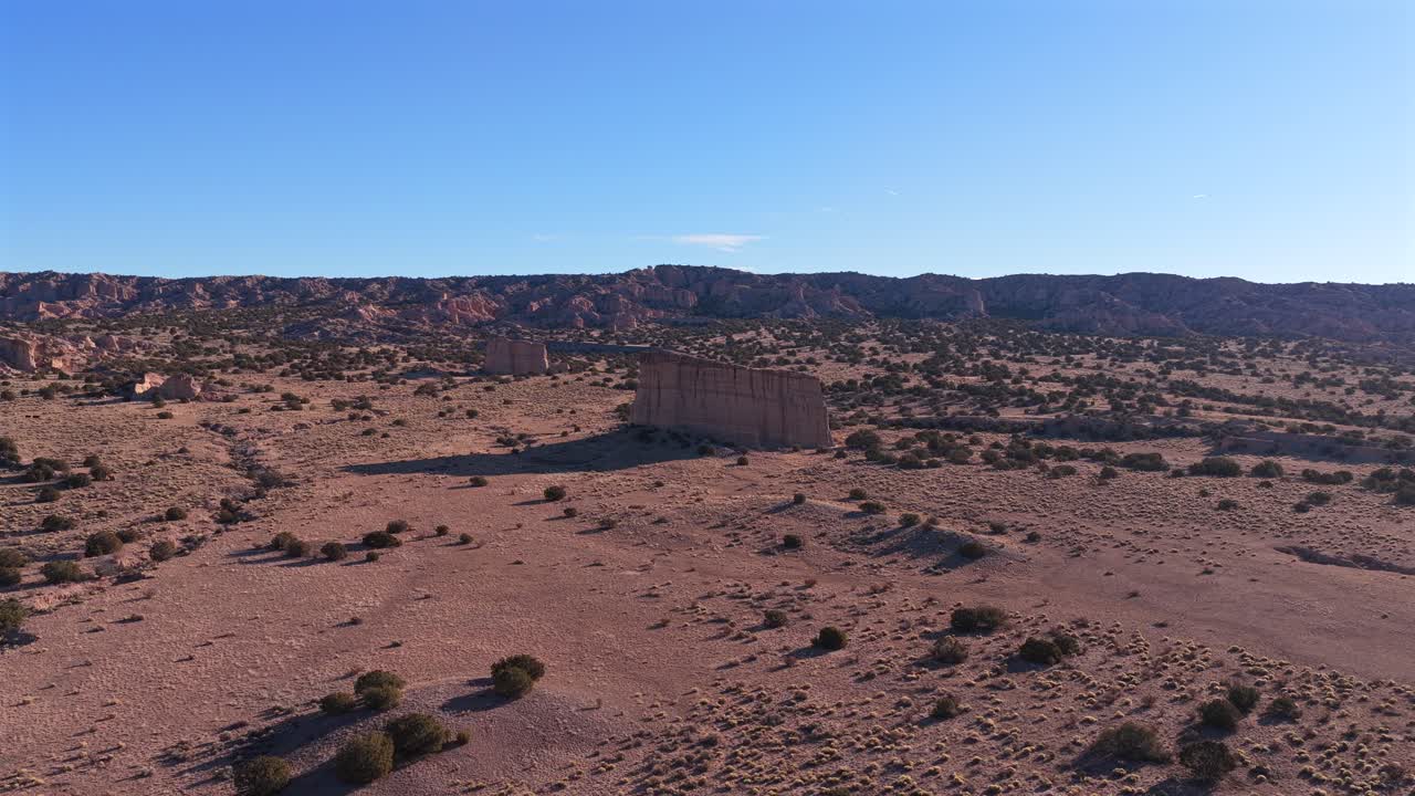 Aerial shot moving directly toward the two striking vertical rock formations, emphasizing their immense scale. This cinematic view is of the rugged high desert in remote Northern New Mexico