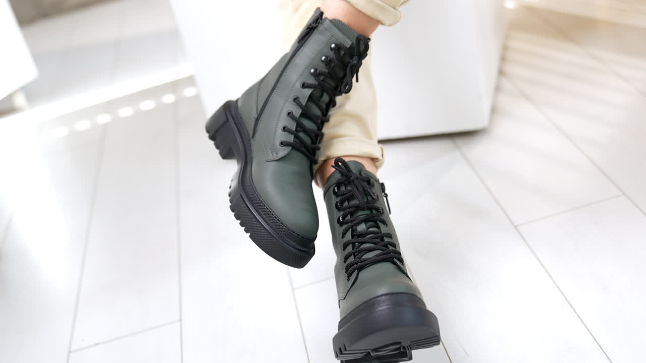 Woman sitting in studio demonstrating grey boots on tractor soles. Beautiful modern footwear at white backdrop. Close up.