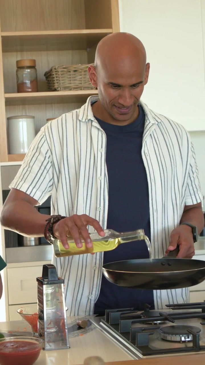 Video verticale: Aprendo la bottiglia dell'olio, uomo in camicia che versa l'olio nella padella sul bancone, cipolla aggiunta.