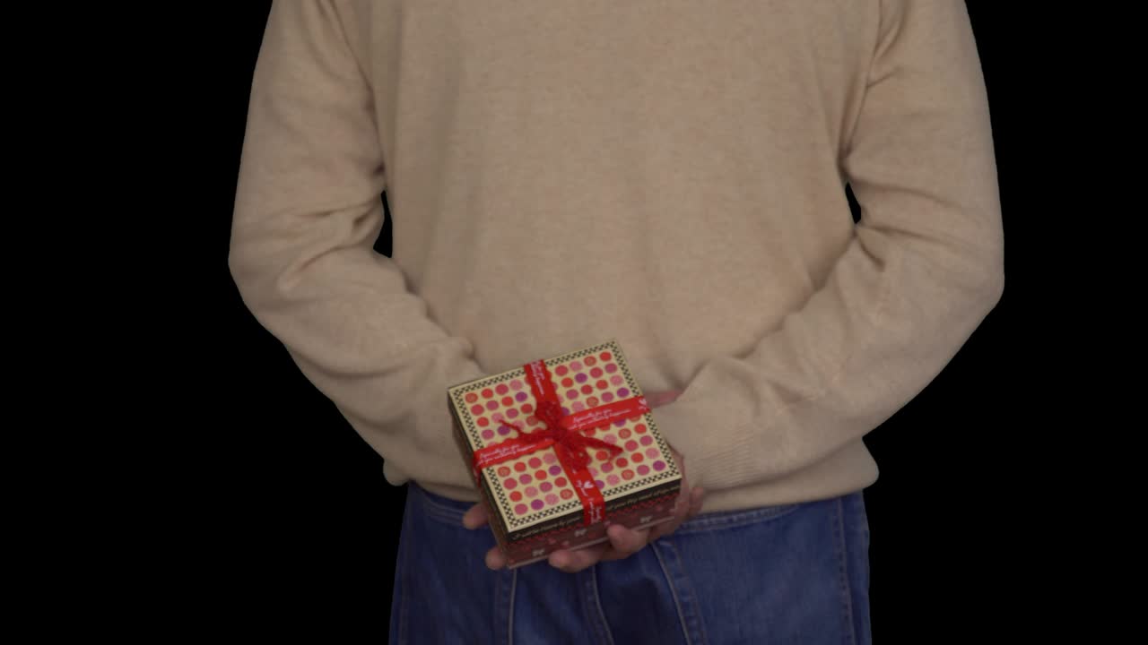청바지와 베이지 스웨터를 입은 백인 남자가 그의 뒤에 선물 상자를 들고있다. 뒤에서 남자의 시야. 남자는 선물을 준다. 알파 채널 크로마 키 투명한 배경. 잠겼다.