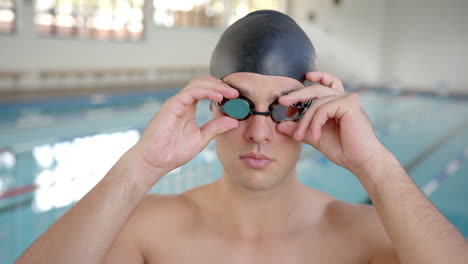 male swimmer adjusting goggles, preparing for training in indoor swimming pool