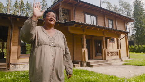 smiling middle aged woman waving while standing in the yard in a sunny morning