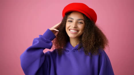 portrait of a smiling woman with curly hair wearing a red beret and purple hoodie