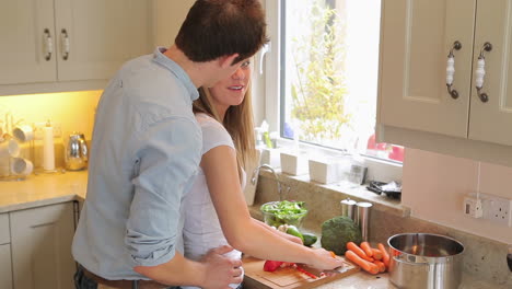 Woman-is-cutting-vegetables-with-man-standing-behind-her