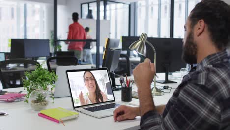 hombre de negocios de raza mixta sentado en un escritorio usando una computadora portátil haciendo una videollamada con una colega